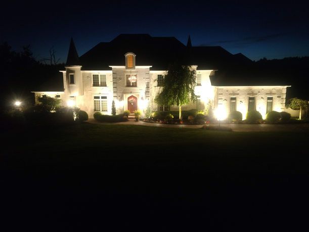 Illuminated large house at night with white exterior and landscaped front yard