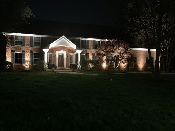 Illuminated brick house at night with white columns and a dark front lawn