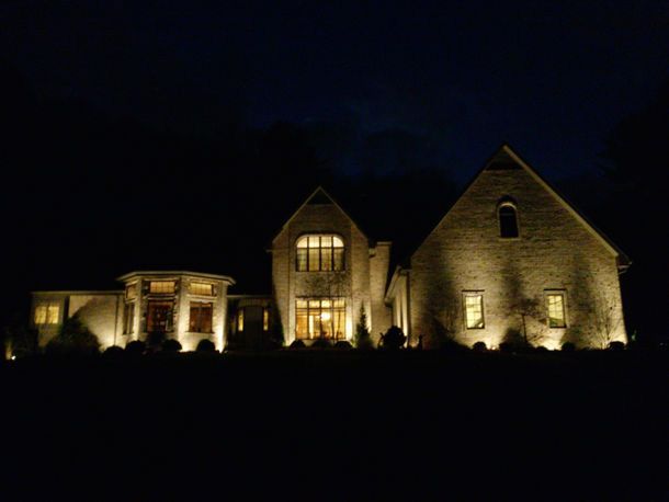 Lit stone house at night with warm exterior lights and dark sky