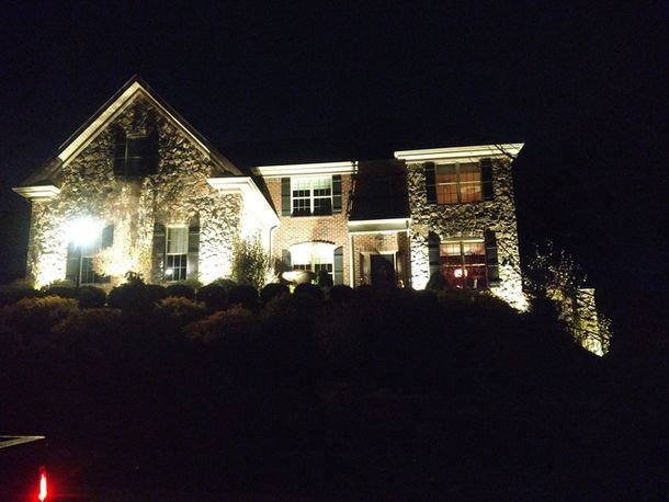 Stone house lit up at night, glowing against a dark sky with shrubs in the foreground
