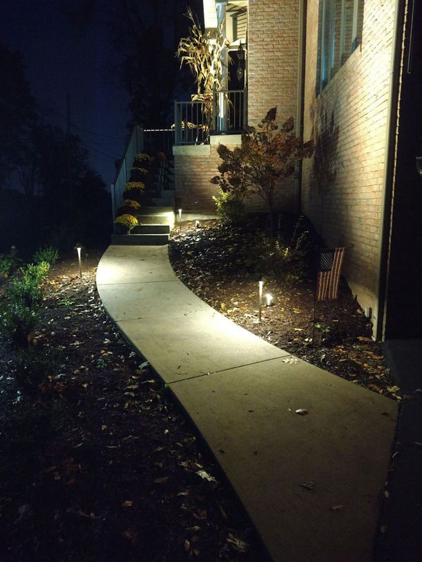 Lit curved walkway beside a brick house at night, illuminated by outdoor lights.