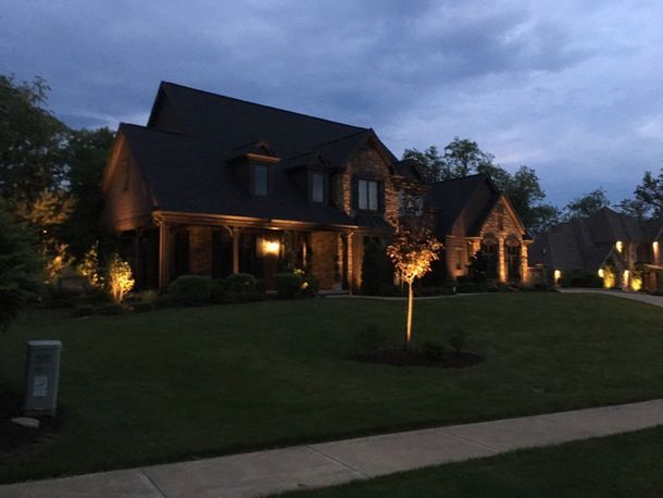 Large brick house with lit windows and porch lights at dusk, viewed from a dark green lawn