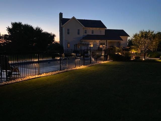 House and fenced backyard lit at dusk, with a pool and dark lawn under a blue evening sky