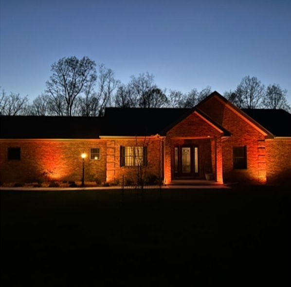 Brick house lit warmly at dusk, with trees silhouetted against a blue evening sky.