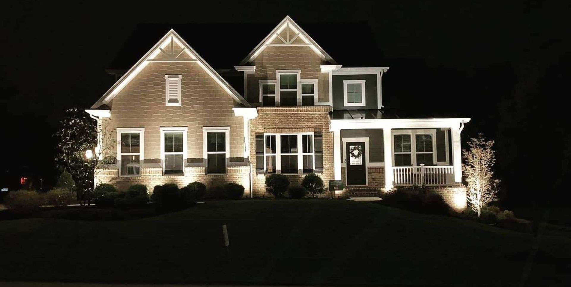Well-lit suburban house at night with a gabled roof and front porch