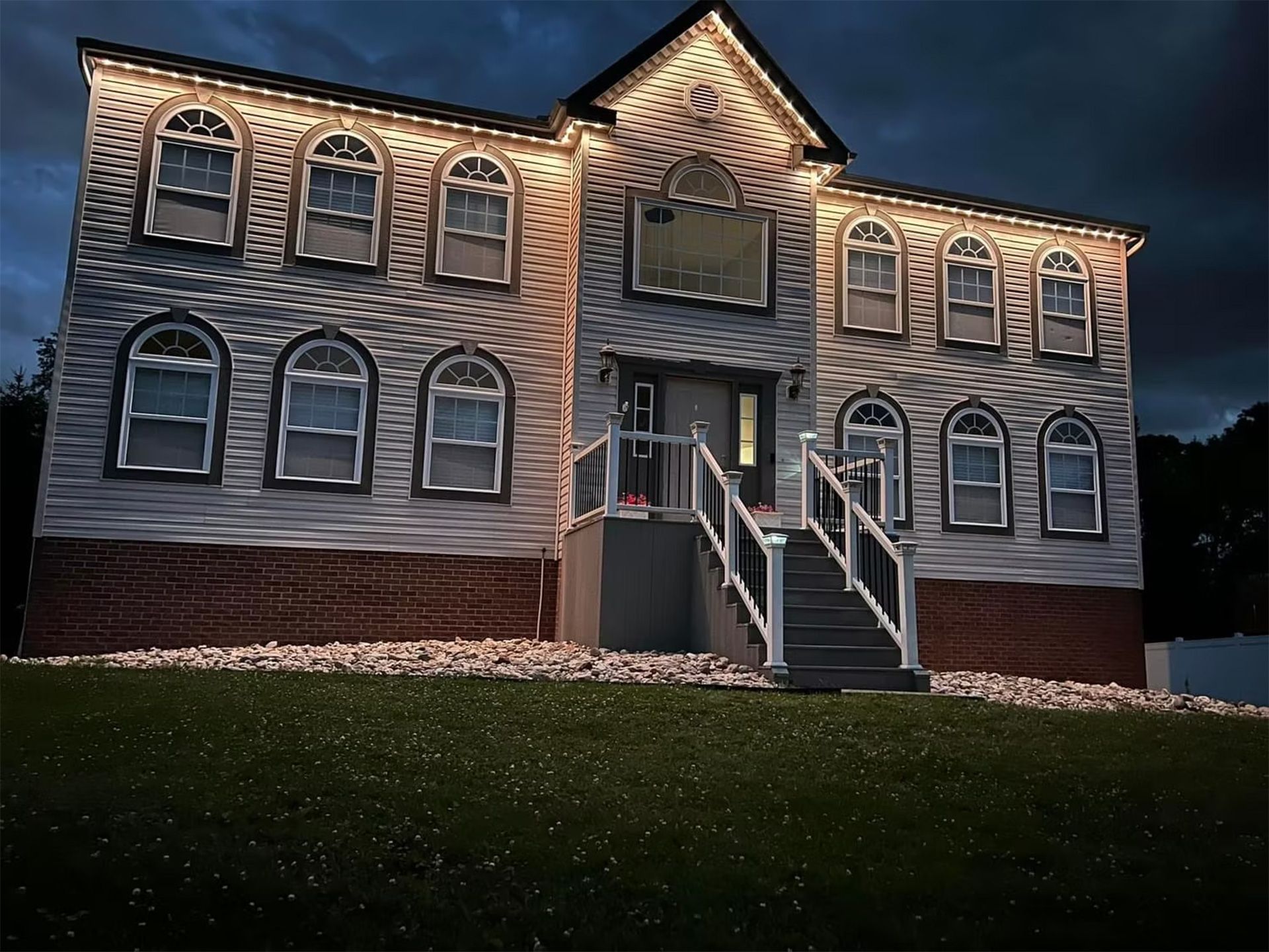 Two-story brick house at dusk with lit windows and front stairs