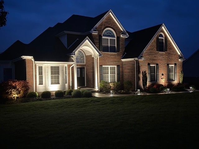 Brick suburban house lit up at night with illuminated windows and manicured lawn.