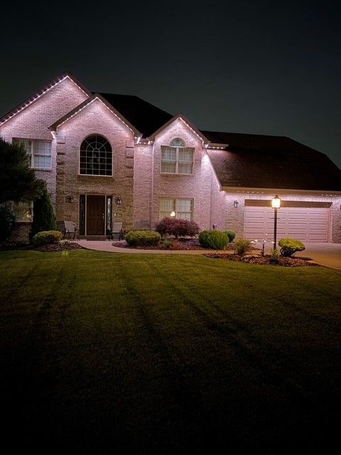 Two-story brick house with lit exterior at night and a dark front lawn