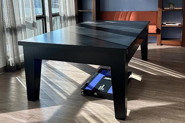 A black pool table is sitting in a living room next to a window.