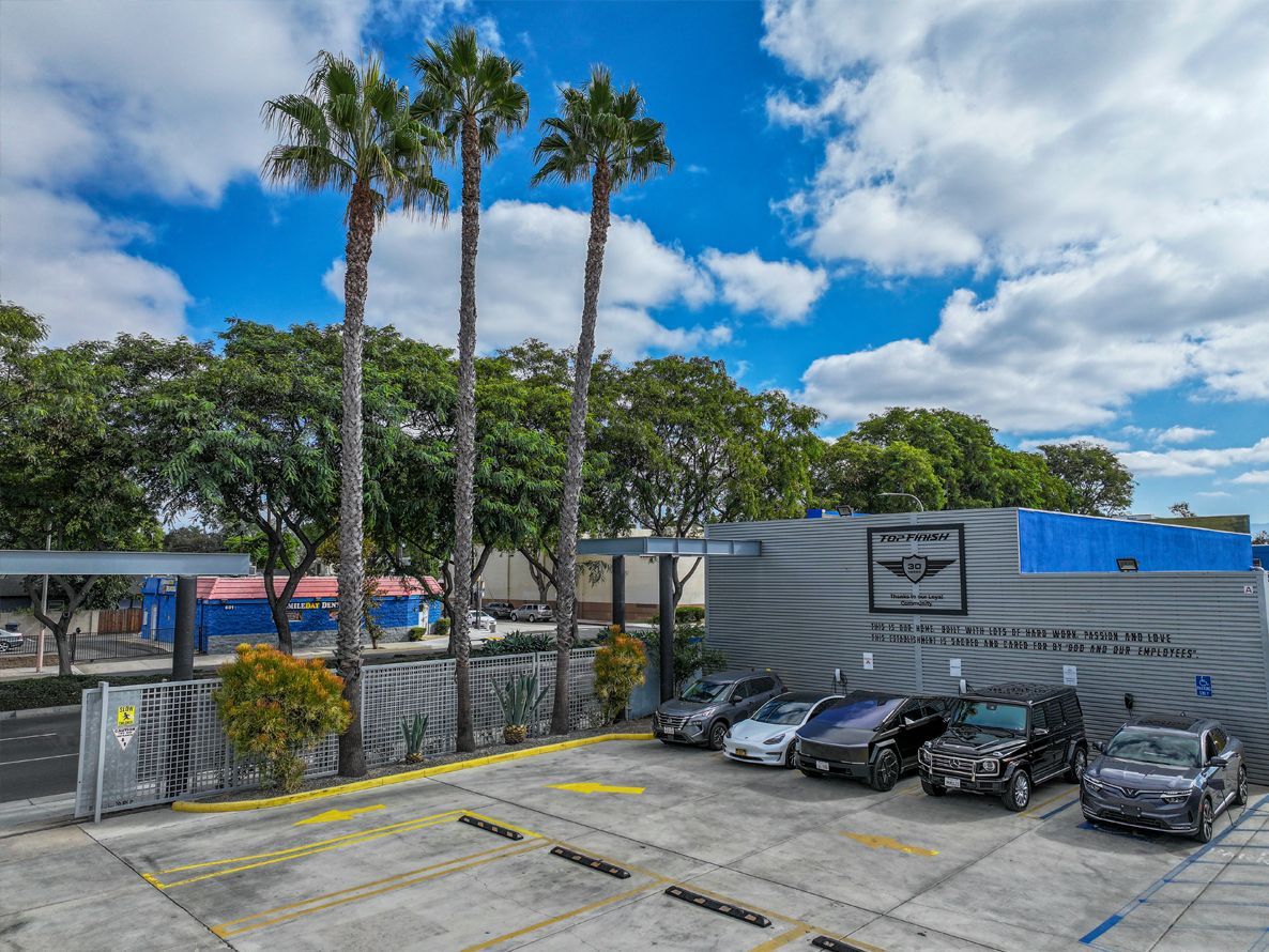 Exterior of a building with palm trees, parked cars, and a blue sky.