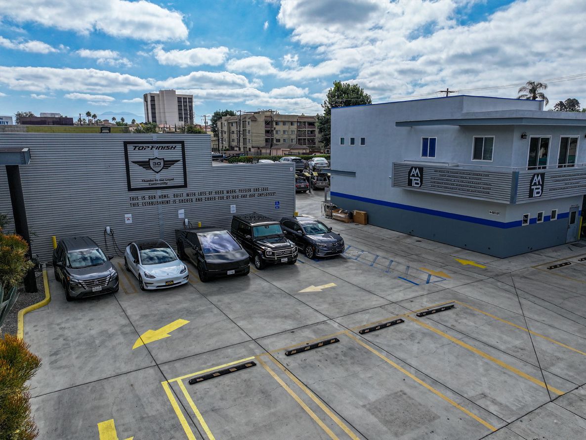 Cars parked outside a building, with a logo, blue and gray tones under a partly cloudy sky.