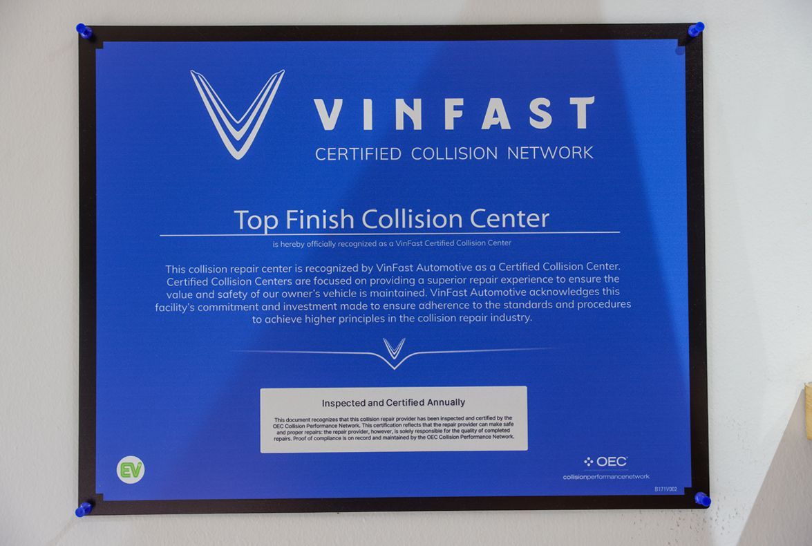 A blue sign for VinFast-certified Top Finish Collision Center with white text and logo, mounted on a wall.