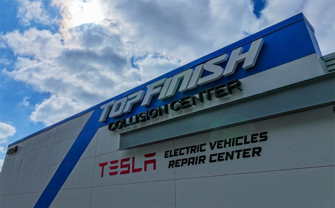 Top Finish Collision Center sign, Tesla electric vehicle repair, blue and white building.
