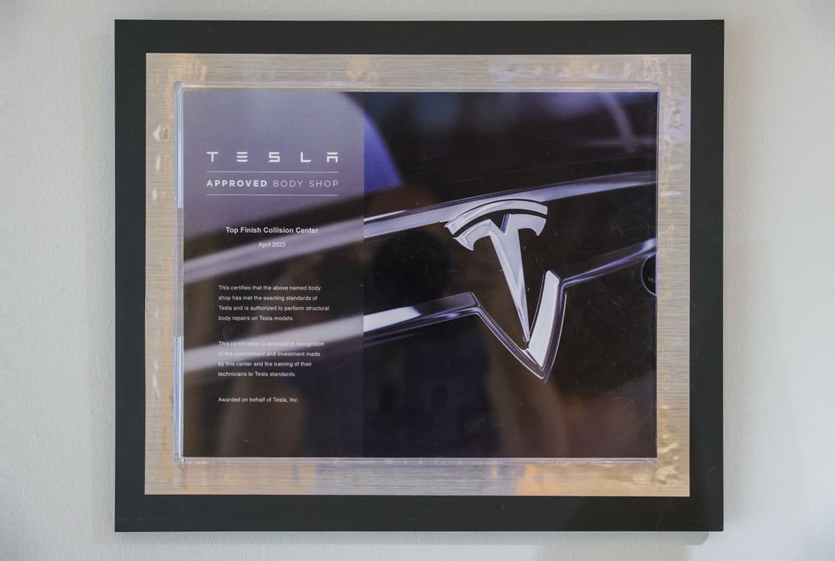 Tesla logo and text in a framed photo. Silver and black frame, hung on a white wall.