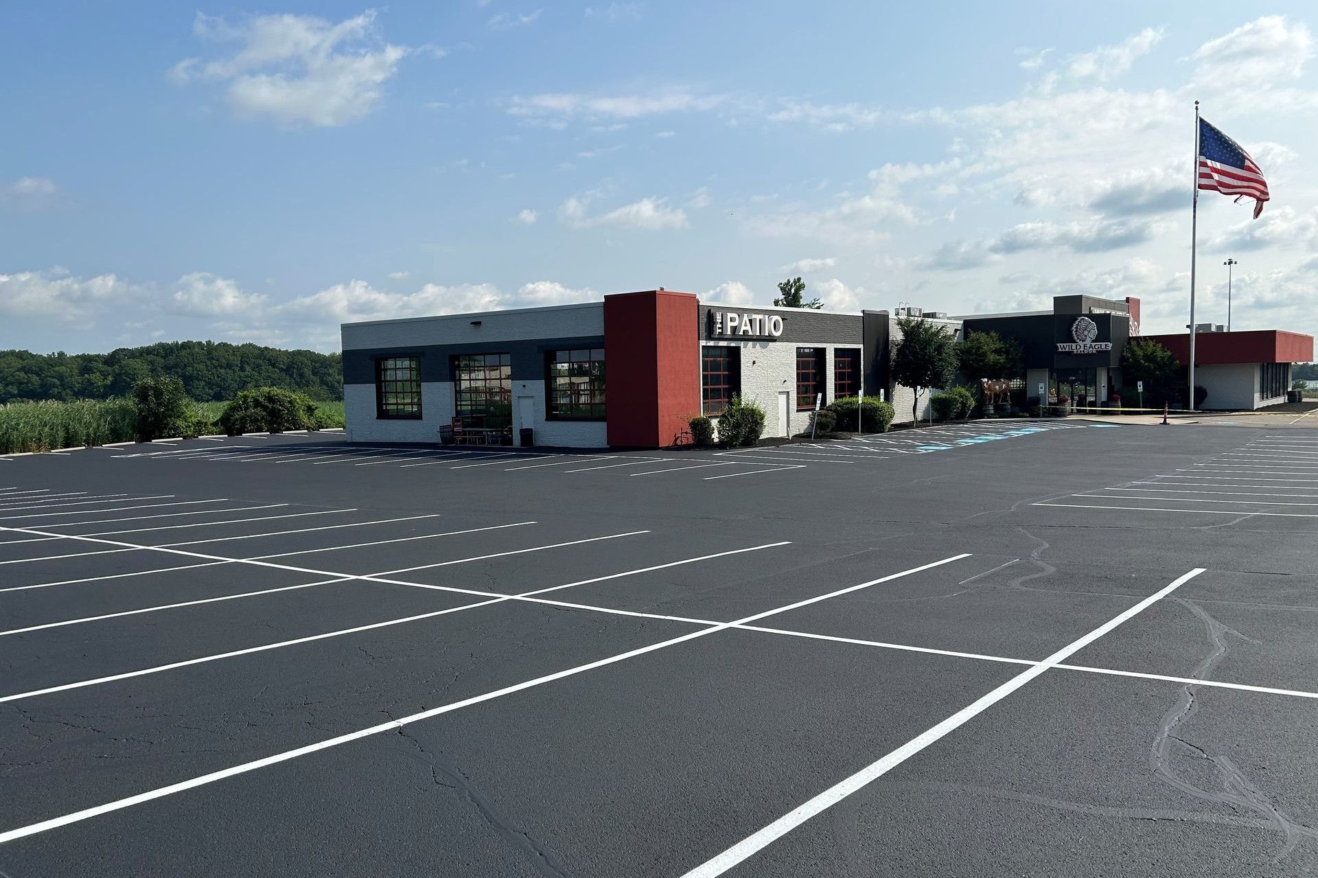 Restaurant with a red and gray facade, large parking lot, and American flag under a blue sky.