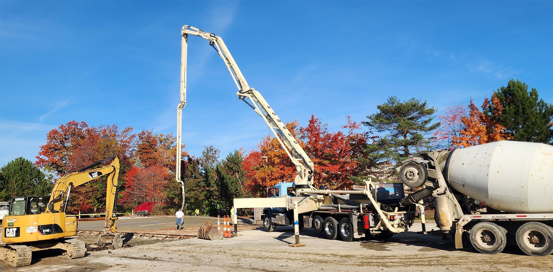 Construction site with a concrete pump and excavator working on a sunny day.