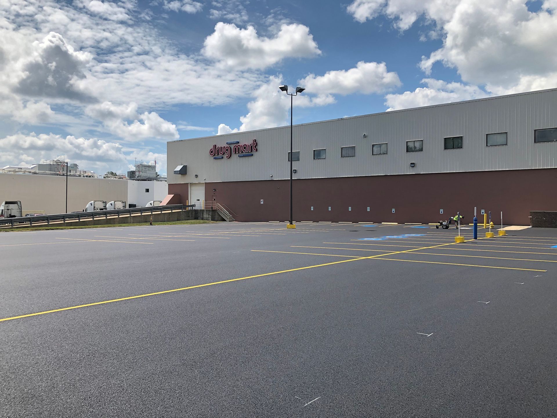 Exterior of a warehouse-like building with a sign on top, brick bottom, and a parking lot on a sunny day.