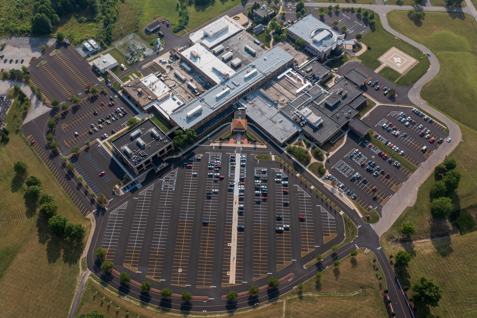 Aerial view of a large hospital complex with extensive parking areas and a rooftop helipad.