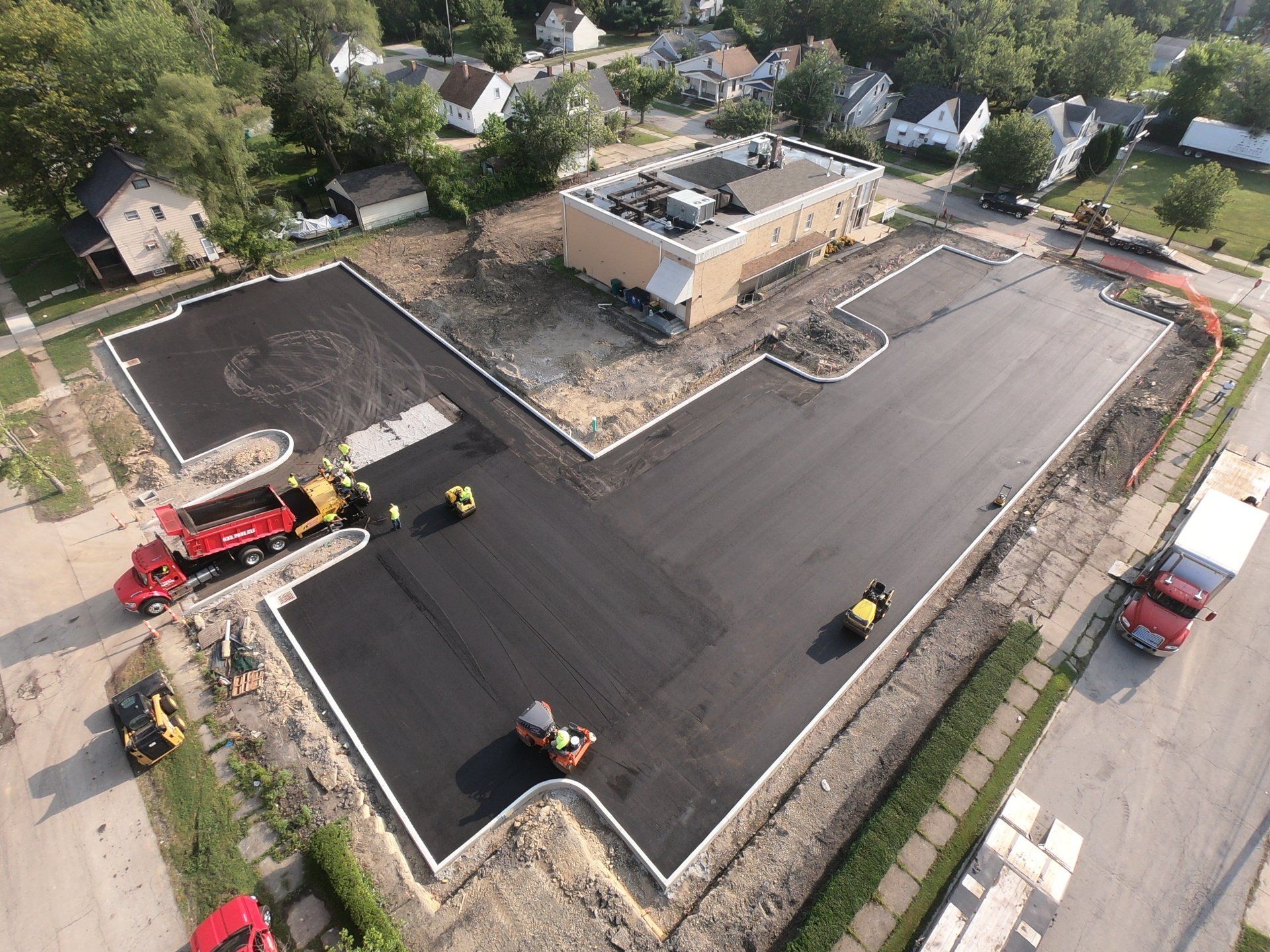 Aerial view of asphalt paving at a construction site with buildings and vehicles.