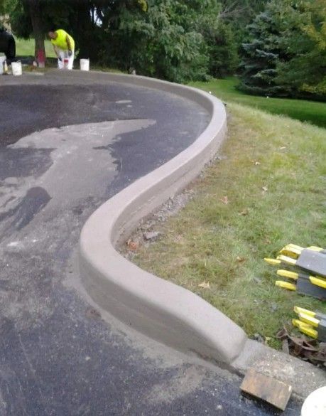 Newly poured concrete curb along a curved driveway; worker in background.
