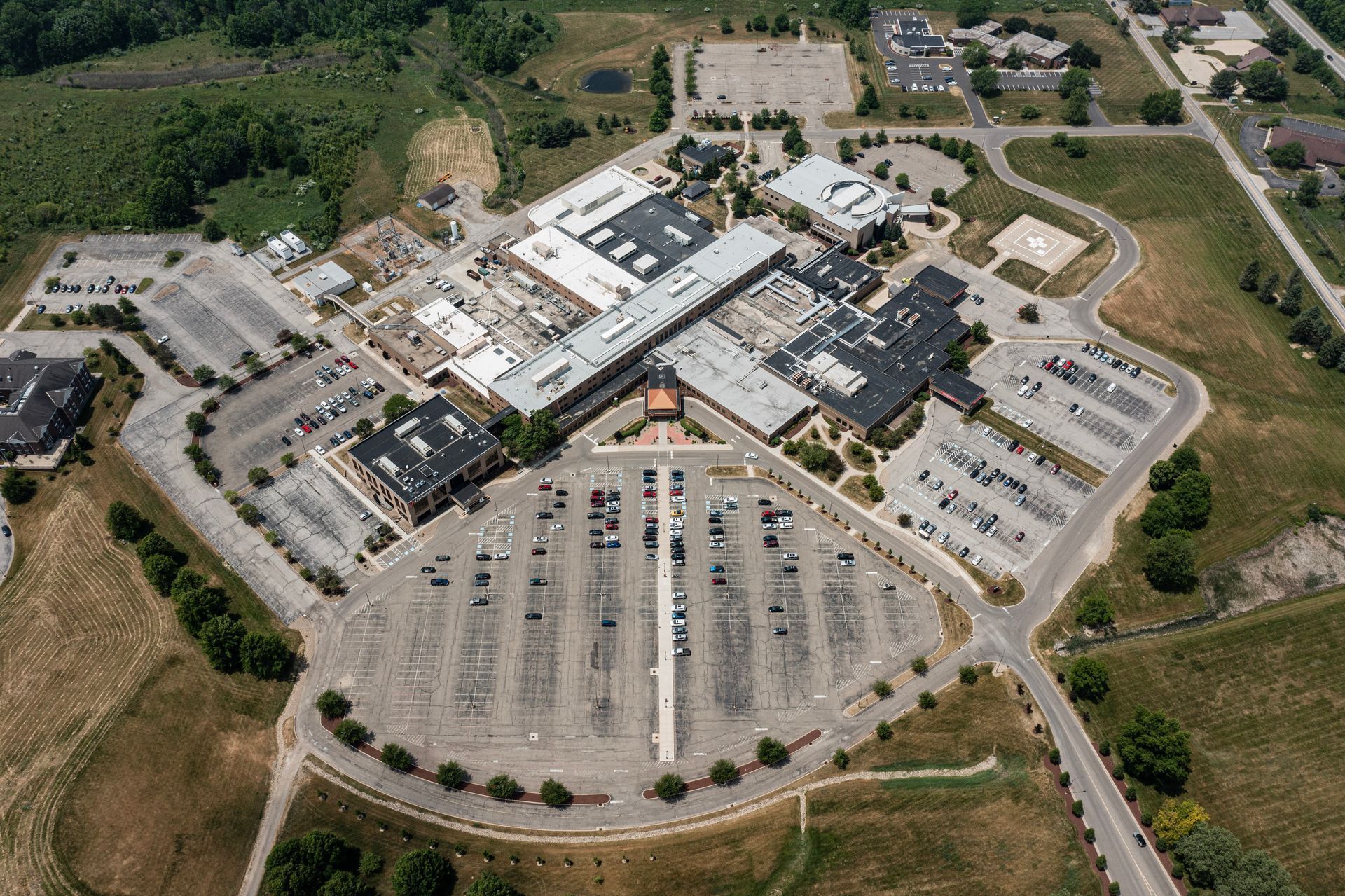 Aerial view of a large hospital complex with extensive parking areas. Buildings are various sizes and shapes.