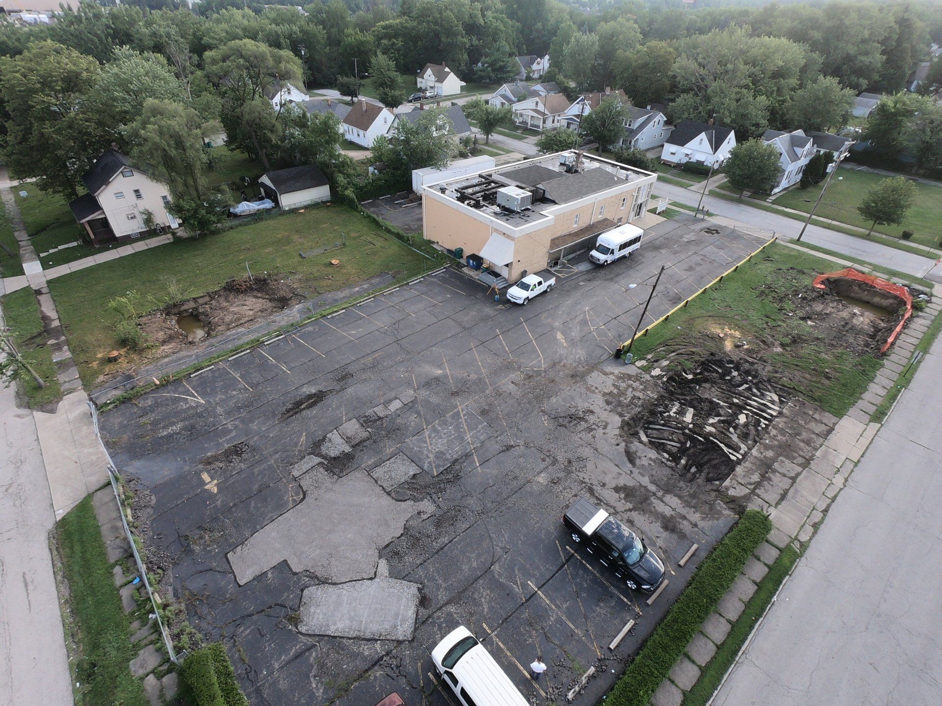 Aerial view of a deteriorating parking lot, adjacent to a building and residential neighborhood.
