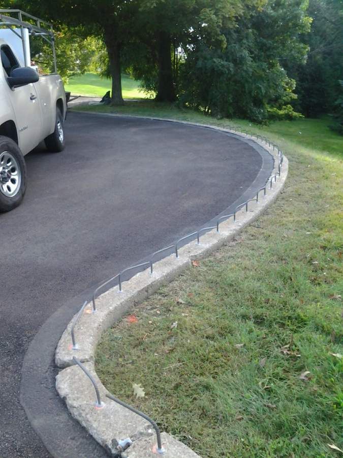 Asphalt driveway with concrete curb under construction next to grass. A silver pickup truck is parked on the driveway.