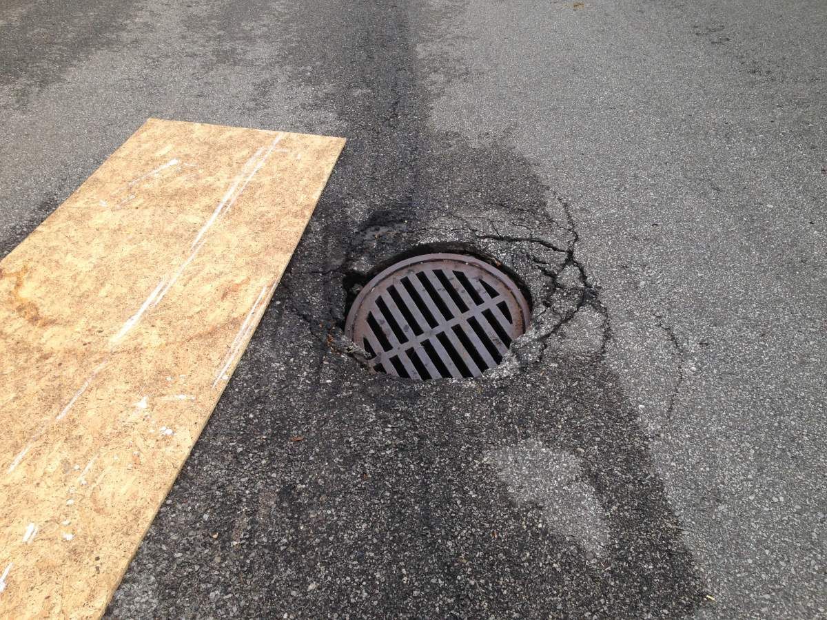 Asphalt driveway with concrete curb under construction next to grass. A silver pickup truck is parked on the driveway.