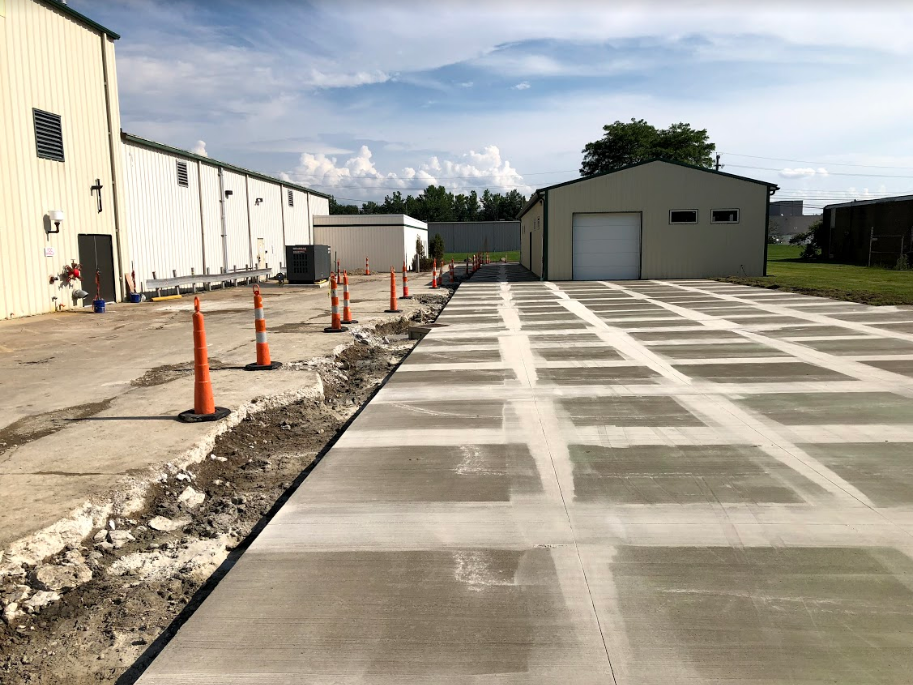New concrete driveway with square grid pattern. Construction cones line the edge near buildings.