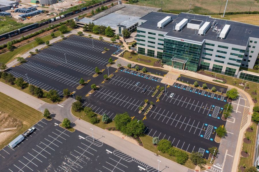 Aerial view of large asphalt parking lots surrounding a modern office building with a glass facade.
