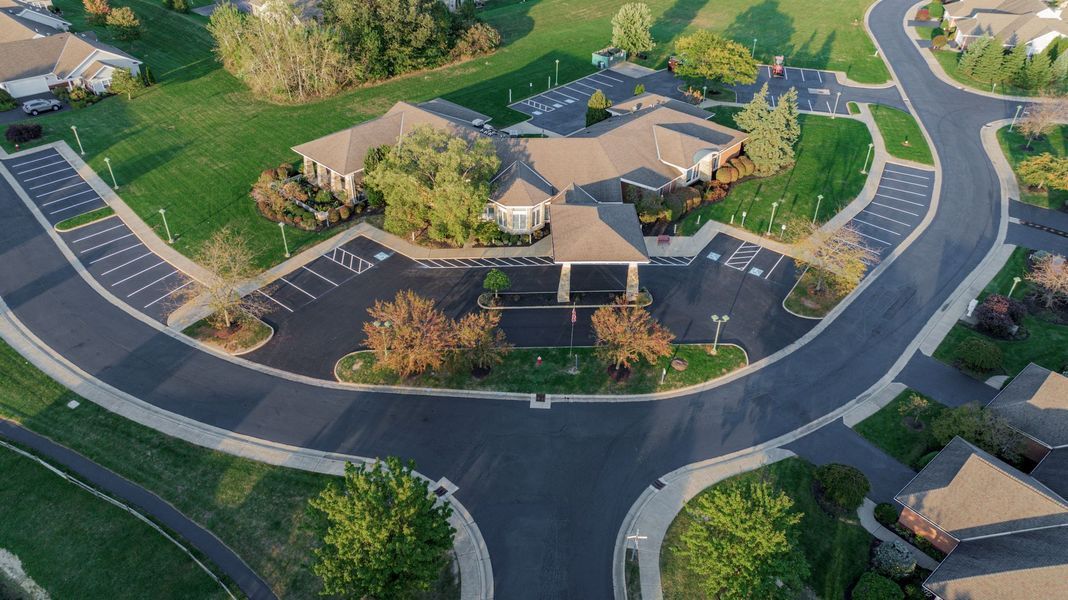 Aerial view of a paved residential road curving around a building with a canopy, surrounded by green lawns and trees.