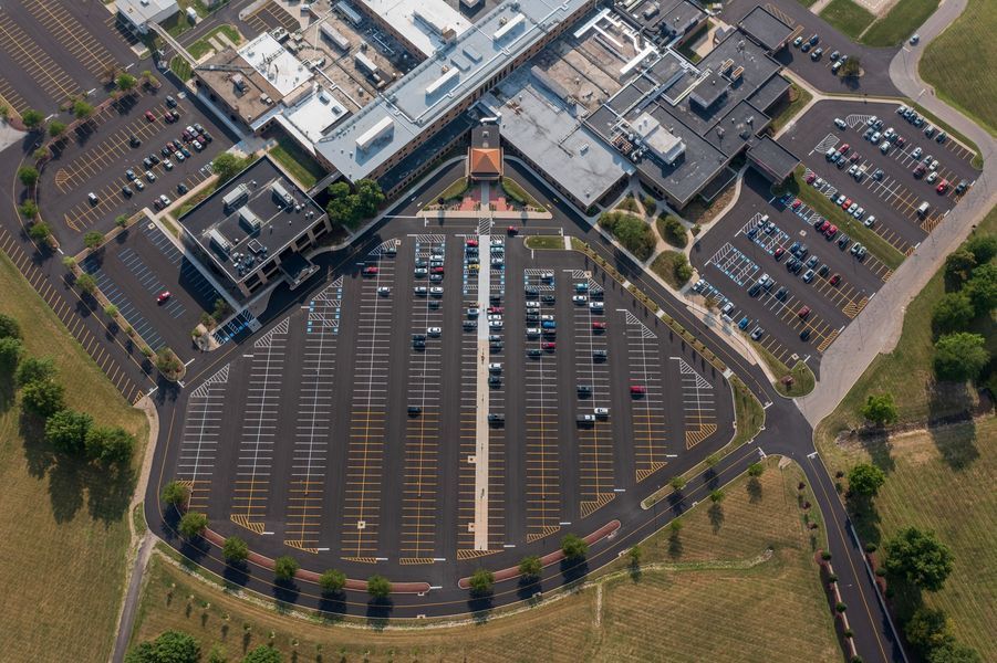 Aerial view of a hospital with multiple buildings, connected to a large parking lot with parked cars.