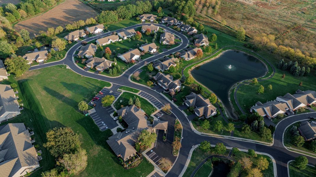 Aerial view of a suburban neighborhood with houses, winding roads, a pond, and green spaces.