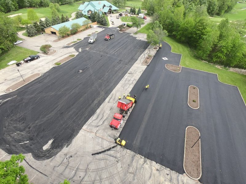 Aerial view of asphalt paving on a parking lot near a building and green landscaping.