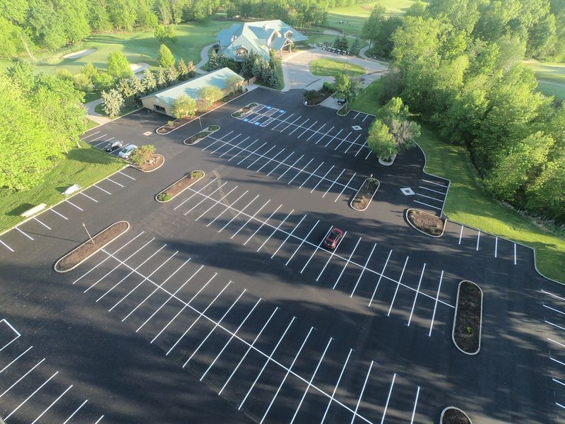 Aerial view of a mostly empty parking lot in front of a building with surrounding trees and greenery.