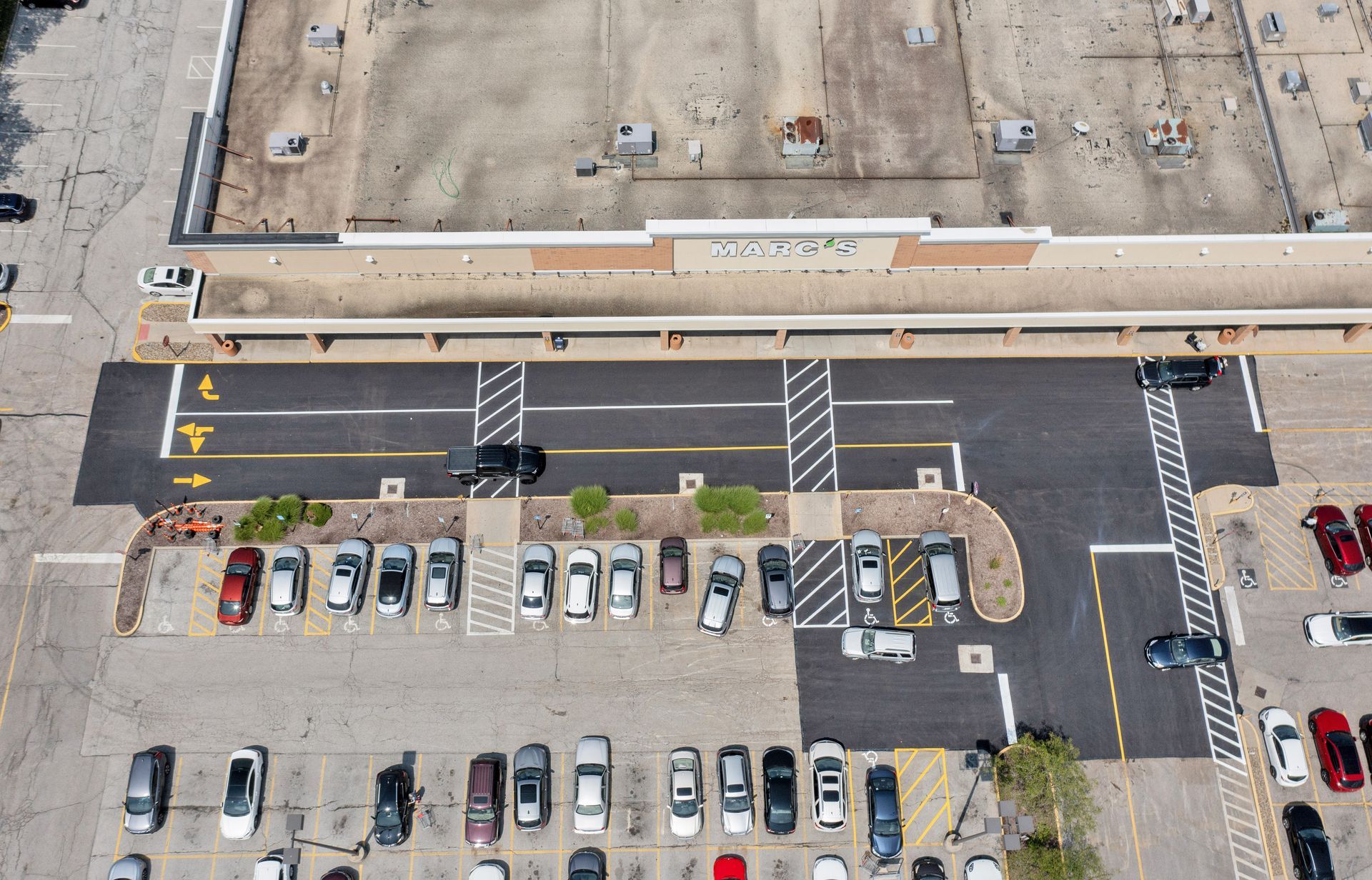 Aerial view of a parking lot and building with cars parked. New asphalt area with crosswalk.