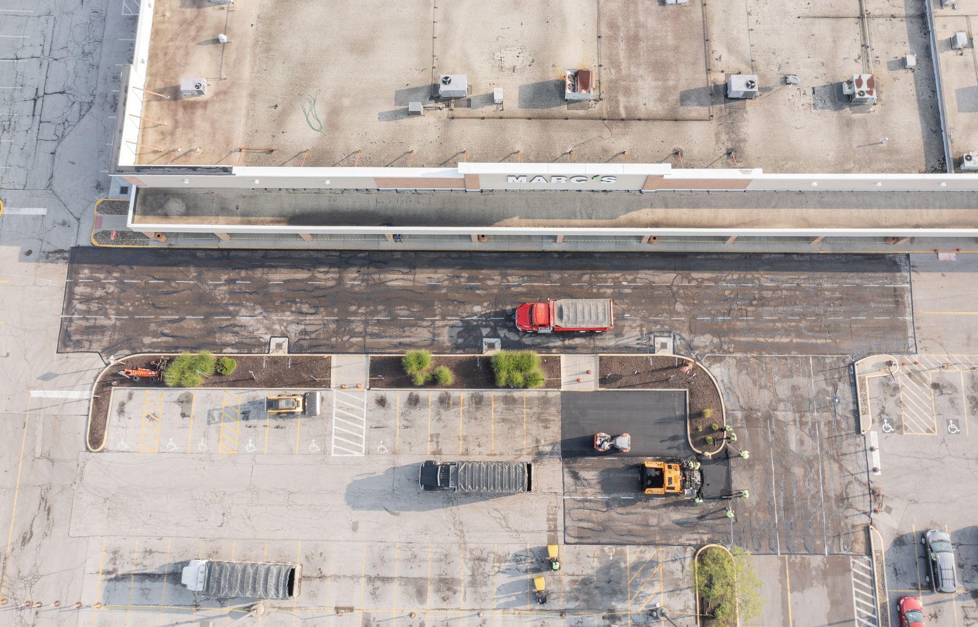 Aerial view of road construction: red truck, machinery, and partially paved area near building.