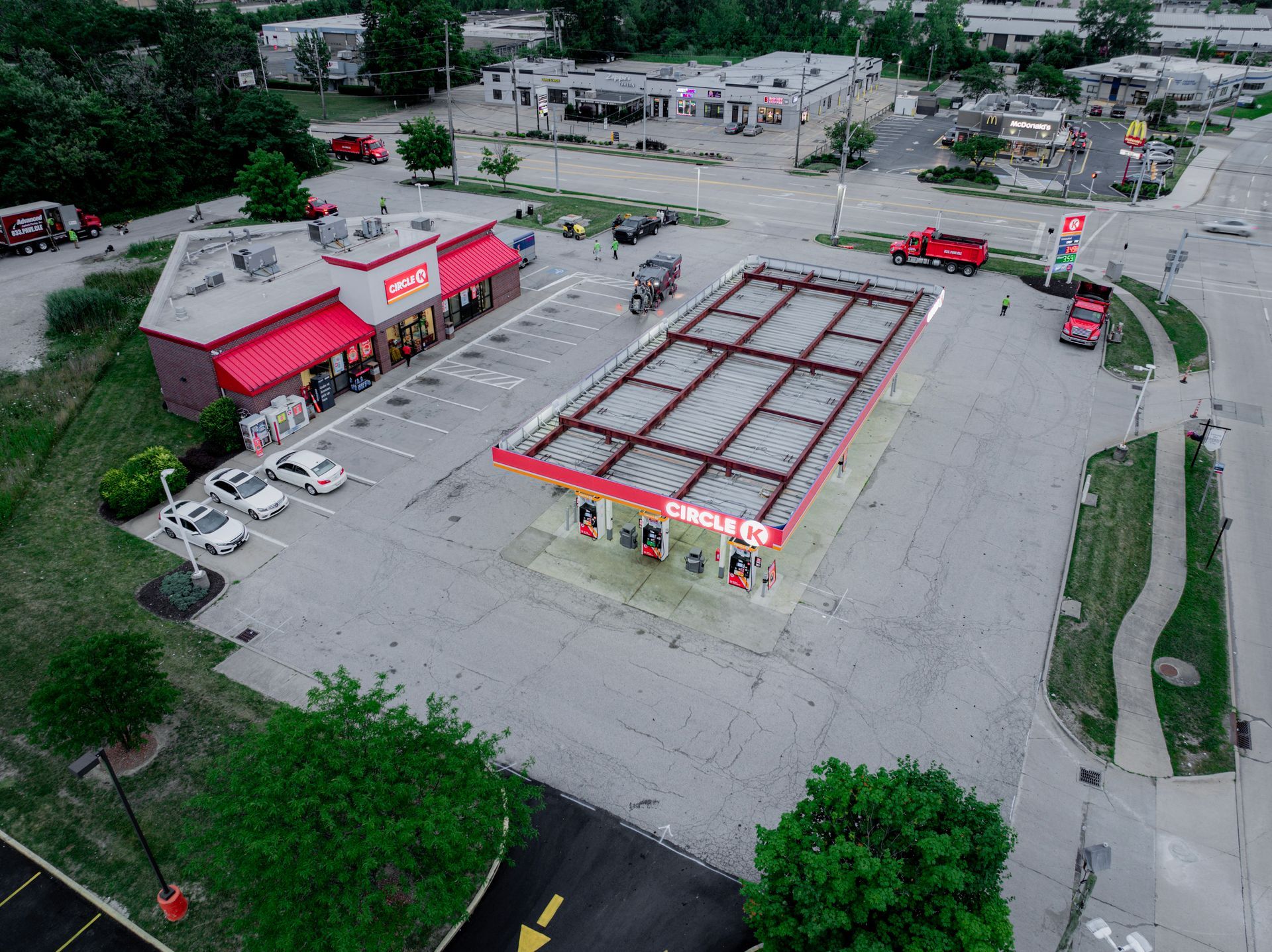 Aerial view of a gas station with a red roof, a convenience store, and parked vehicles. Fire trucks on the right side.