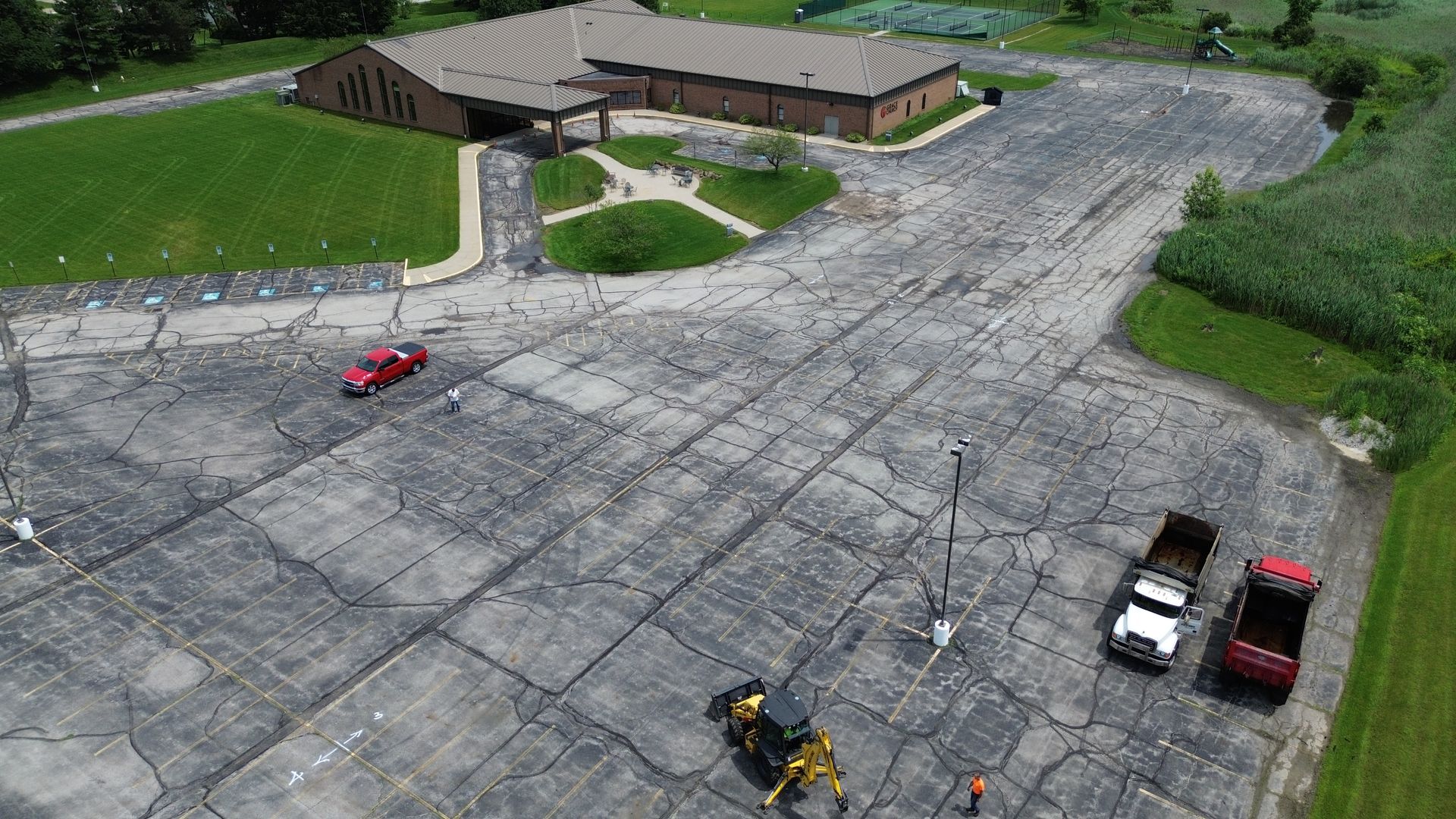 Building and parking lot with construction vehicles, a red car is parked.