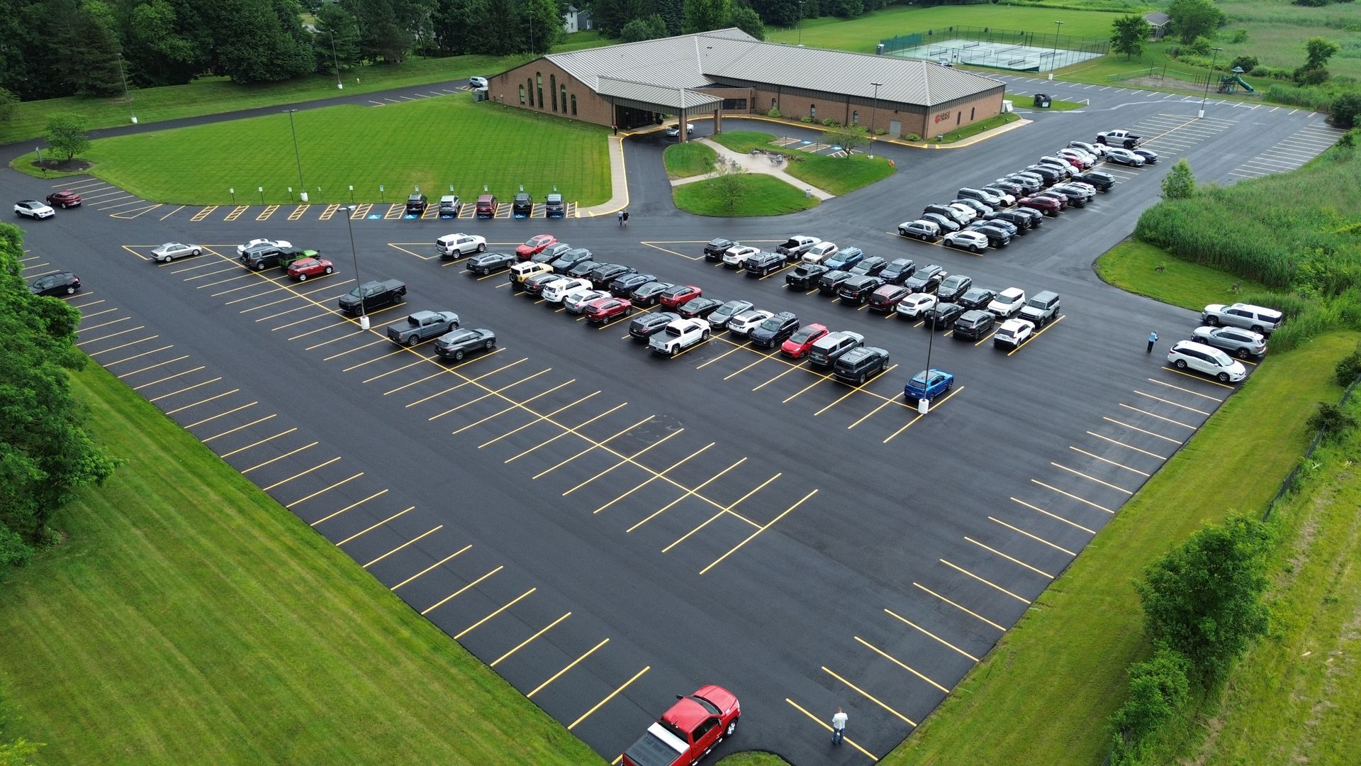 Asphalt road with yellow crosswalk lines, leading up a slight incline past trees and a building.