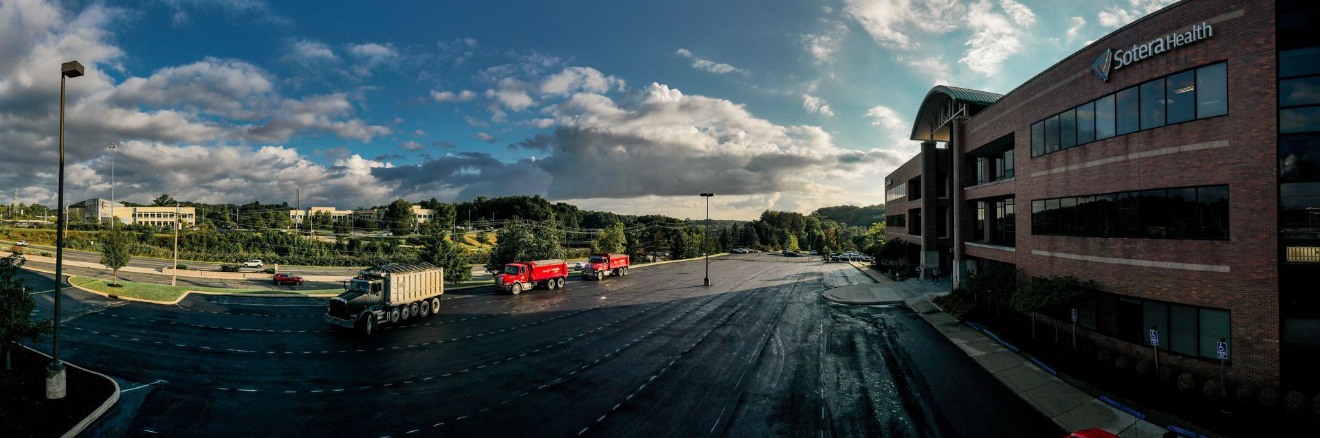 Trucks parked in a lot in front of a modern brick office building on a cloudy day.