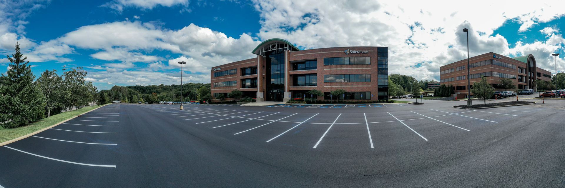 Office building with large parking lot under a cloudy sky.