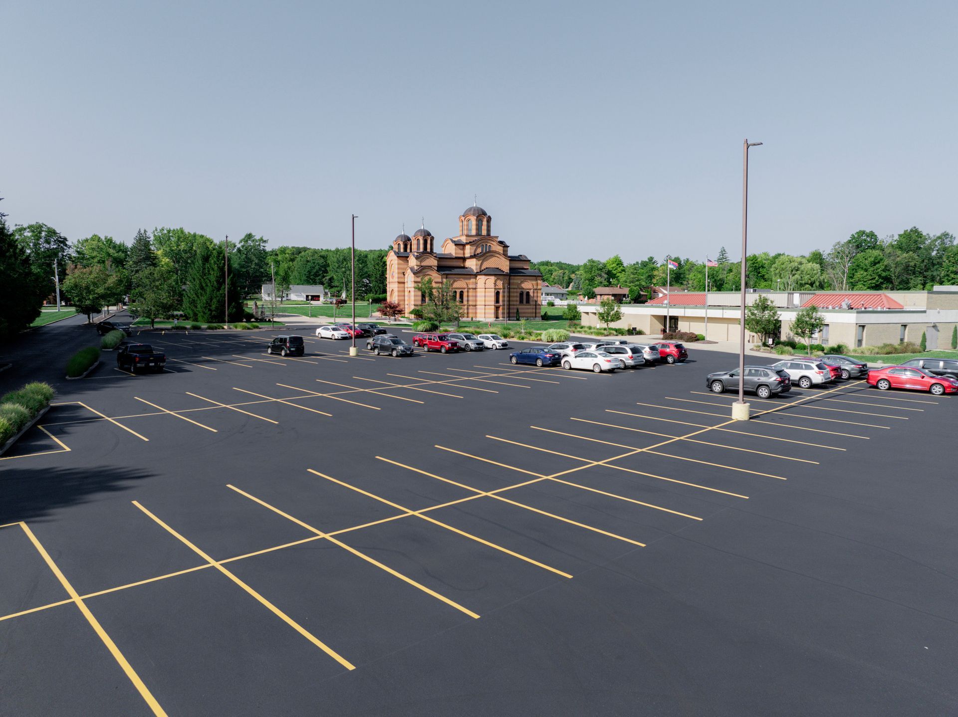 Large asphalt parking lot with parked cars, a brick church in the background, and blue sky.