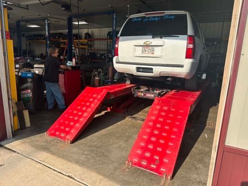 White SUV on red ramps in an auto shop, with a mechanic working nearby.