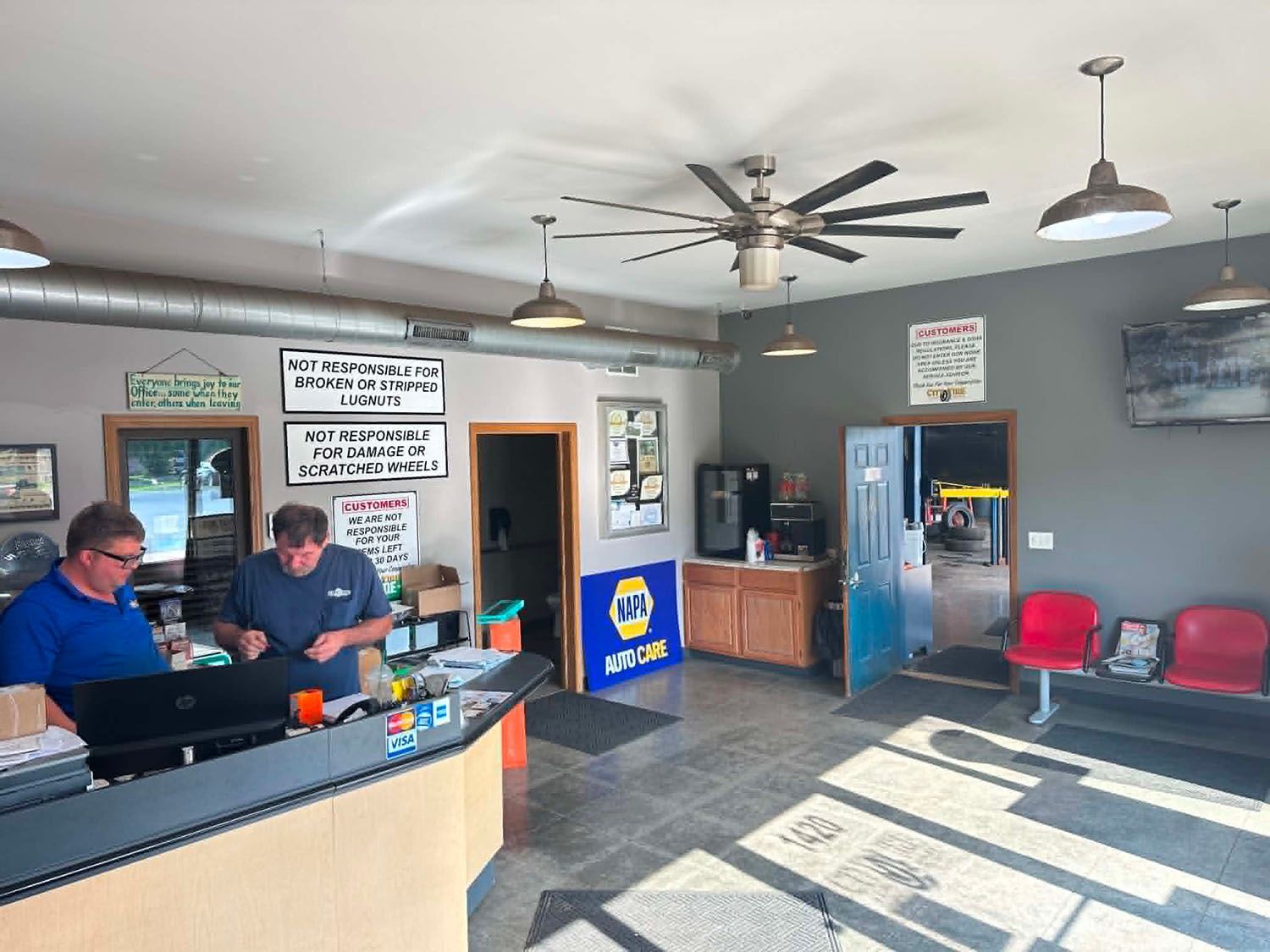 Two men at a bar counter in a casual room with ceiling fans, chairs, and a doorway to a back area.