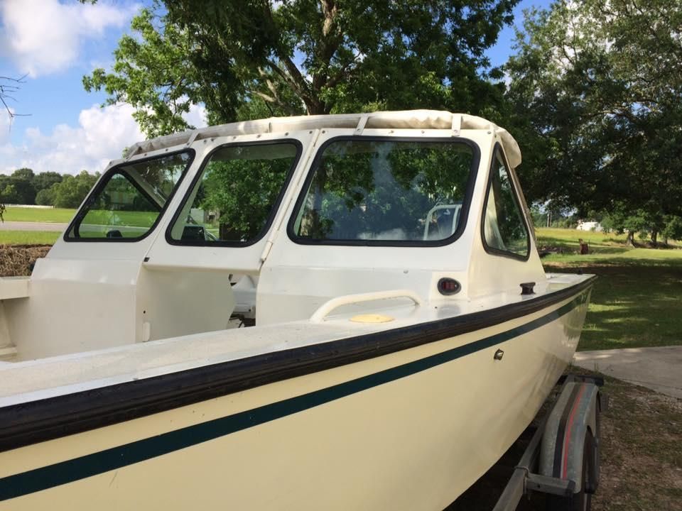 A white boat is parked on a trailer with trees in the background.