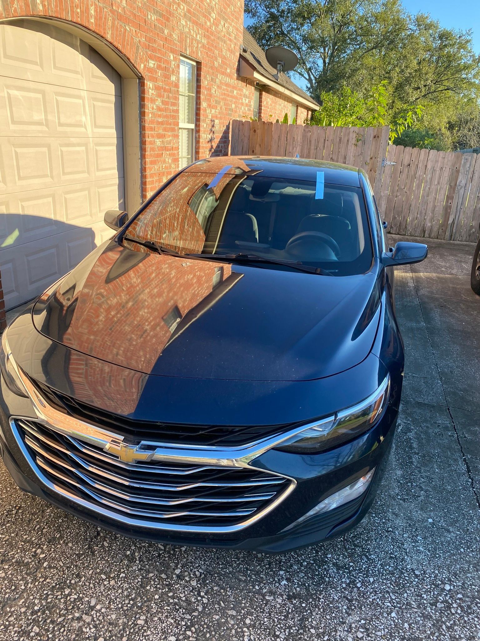 A black car is parked in a driveway in front of a brick house.