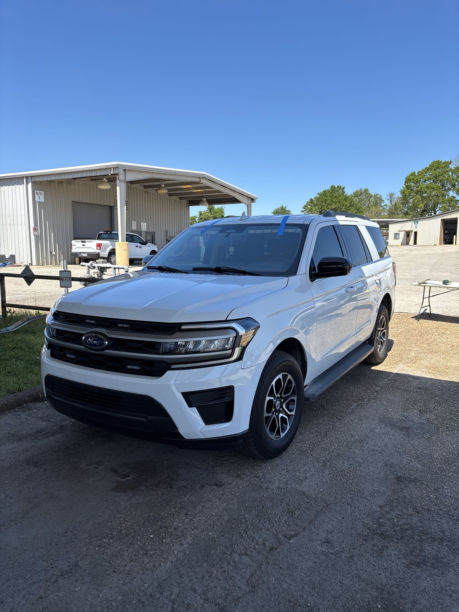 A white ford expedition is parked in a gravel lot in front of a building