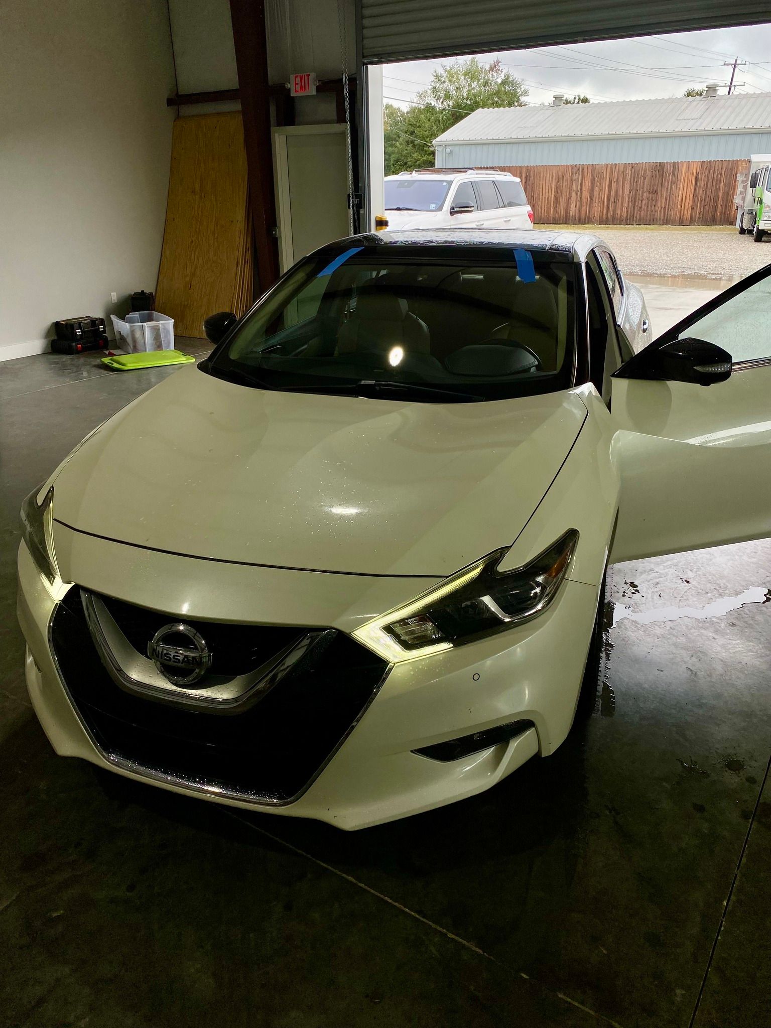 A white nissan maxima is parked in a garage with its doors open.