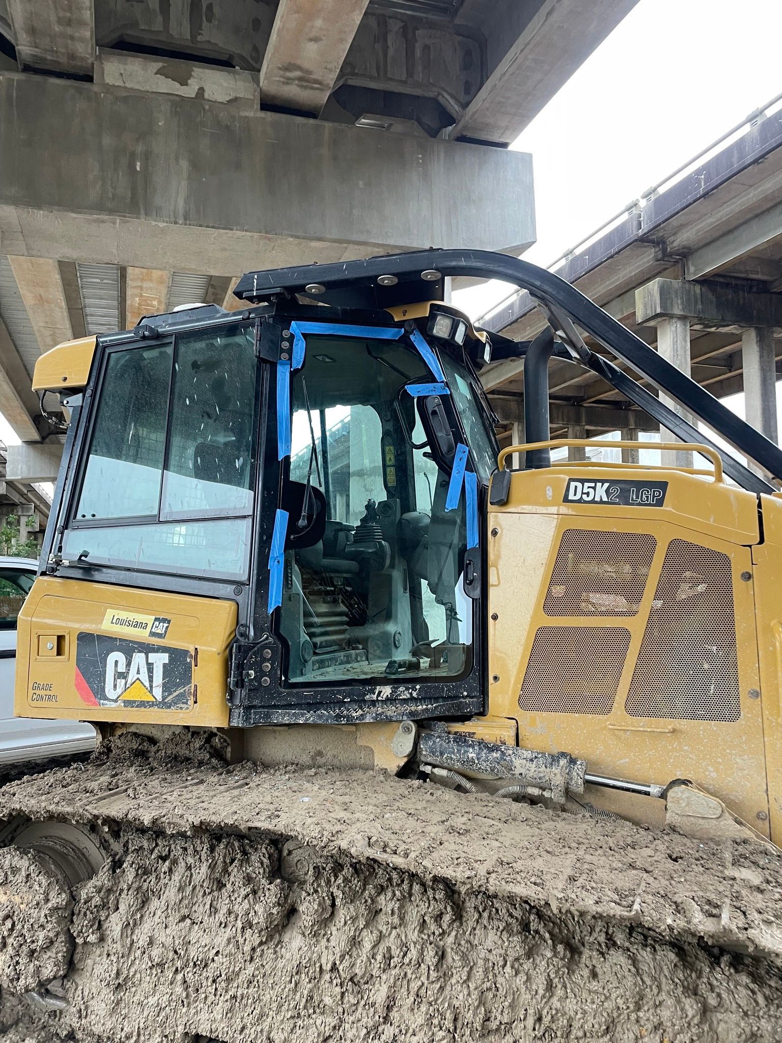 A cat bulldozer is sitting under a bridge in the mud.